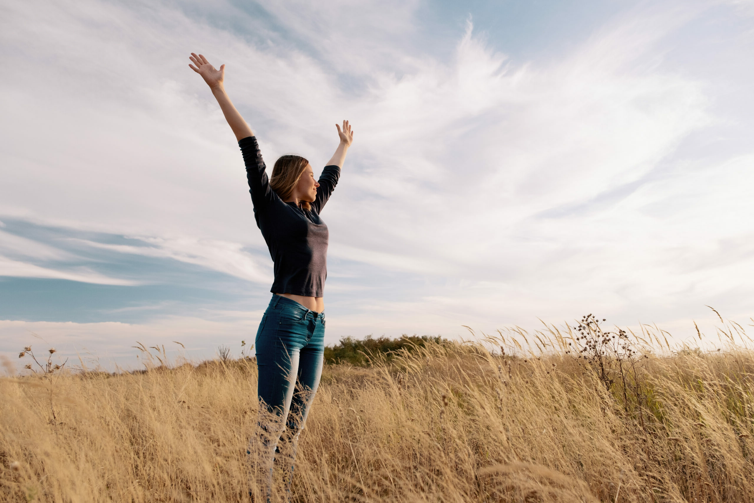 Young happy woman in a golden field on sunset.